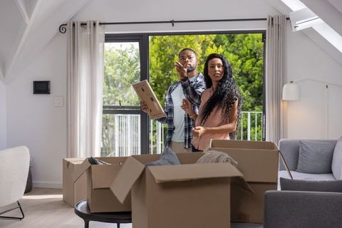 Young african american couple unpacking boxes in bright modern living room with balcony