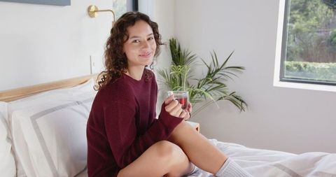 Woman relaxing on bed with hot beverage in bright cozy bedroom