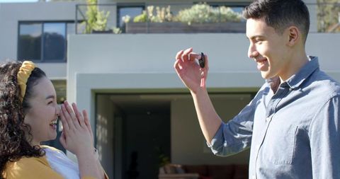 Couple exchanging keys in front of modern suburban home