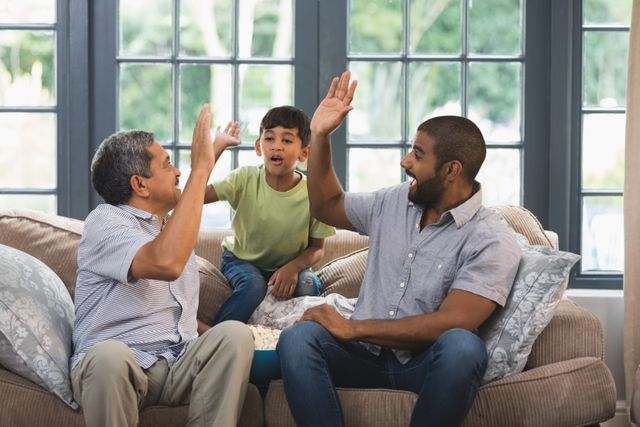 Multi-generation family giving high five while sitting together on couch at home