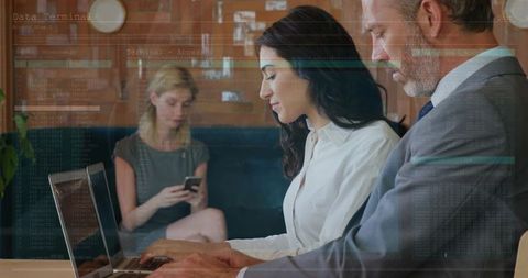 Business professionals collaborating over laptop in lounge with code overlay concept