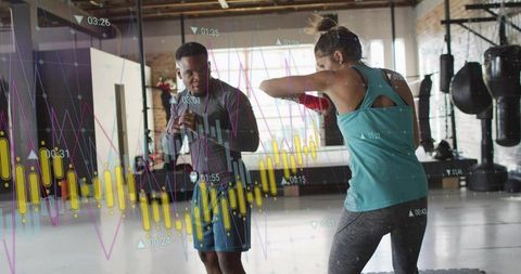Female boxer throwing punch during coach-led training in industrial gym studio