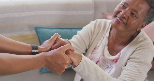 Mid section of female doctor holding hands and supporting african american senior woman at home. medical healthcare concept