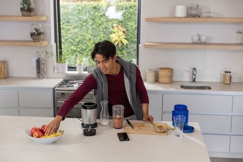 Asian man preparing healthy smoothie at modern kitchen island with fresh fruit and blender