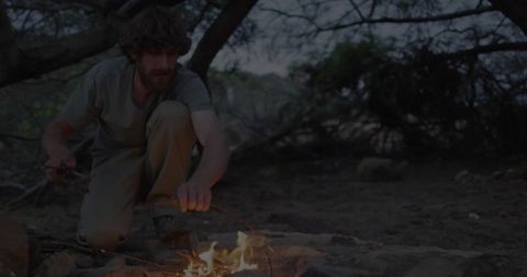 Man Tending Campfire in Forest Clearing Amidst Wilderness