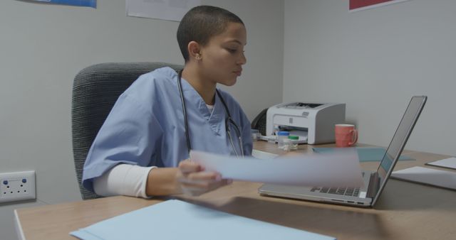 Focused nurse reviews patient documents at her office desk. She's engaged in her work, ensuring accuracy and care in a healthcare setting.