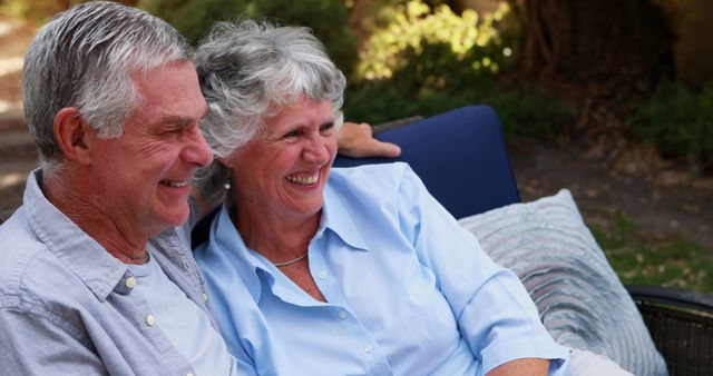 Senior Caucasian couple enjoys a relaxed moment outdoors, with copy space. They share a laugh, showcasing a warm, loving relationship in a serene setting.