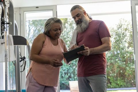 Mature couple reviewing tablet workout plan in sunlit home gym near garden