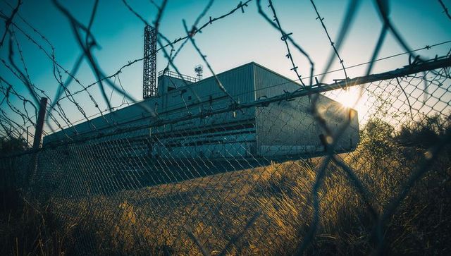 Barbed chain-link fence enclosing industrial site at sunset