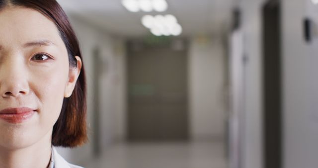 Close-up of a confident female doctor in a modern hospital corridor. She is dressed in professional attire, partly visible with a calm expression. Ideal for healthcare, professional medical staff, and hospital-related content.