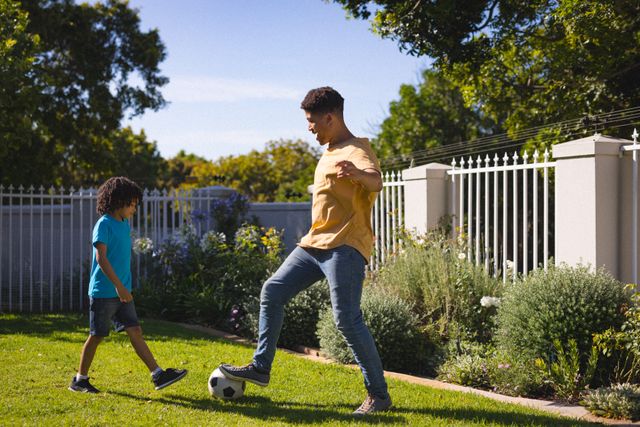 Hispanic father and son enjoying a sunny day by playing soccer together in their backyard. This image can be used to depict family bonding, outdoor sports, weekend activities, and the joy of spending quality time together. Perfect for advertisements or articles related to family life, fitness, and summer fun.
