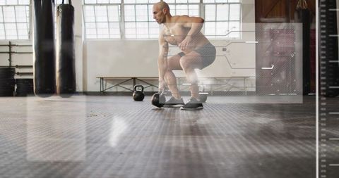 Squatting male athlete reaching for kettlebell in industrial gym during strength training