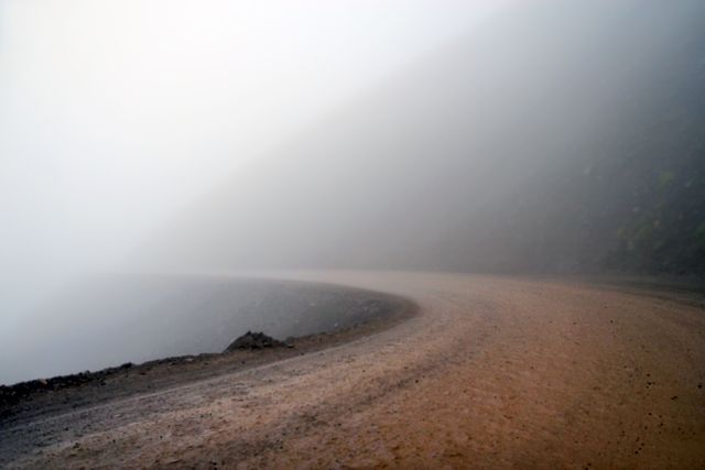 Misty mountain road disappearing into dense fog creates a mysterious and eerie atmosphere. Ideal for travel blogs, adventure websites, or environmental awareness campaigns. Perfect for adding ambiance to design projects or illustrating weather conditions.