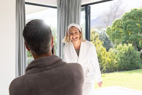 Middle-aged couple enjoying sunny morning at patio door woman in white bathrobe smiling