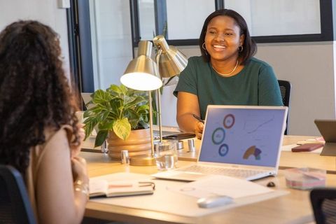 Smiling woman reviewing laptop analytics while collaborating with coworker in modern office
