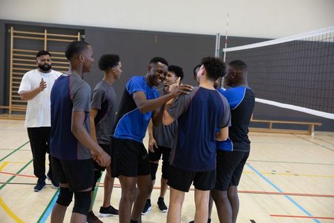 African american male volleyball team celebrating win indoor teammates huddling smiling