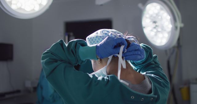 Surgeon adjusting cap and tying back mask under bright lights in a hospital operating room while preparing for an operation. Ideal for use in medical-related content, articles on surgery preparation, healthcare advertisements, and illustrations of hospital environments.