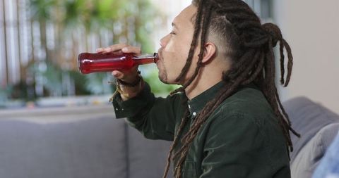 African american man with dreadlocks sipping red beverage on modern living room couch