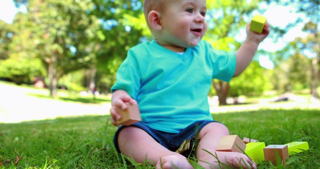 Baby is sitting on grass, playing with colorful blocks. Baby looks joyful, enjoying sunny day in park. Can use for parenting blogs, children's toy advertisements, articles on child development and outdoor activities for infants.