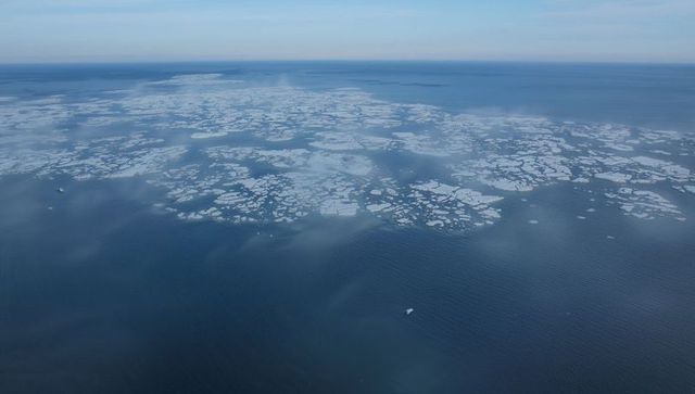 Aerial view of patchy sea ice floes drifting over dark ocean with small vessel and mist
