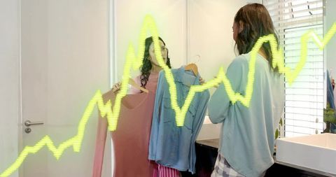 Holding dress and blouse, two women comparing outfits in mirror with neon zigzag overlay