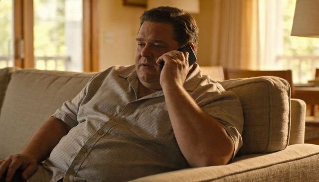Adult man talking on smartphone while relaxing on beige sofa in sunlit living room