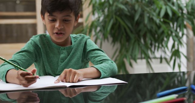 This image shows a young boy focused on his homework, studying at home while wearing a green shirt. Ideal for educational materials, school-related websites, parenting articles, or academic advertisements discussing home learning.
