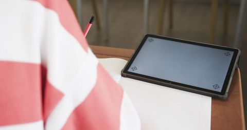 Child writing in classroom using notebook and tablet