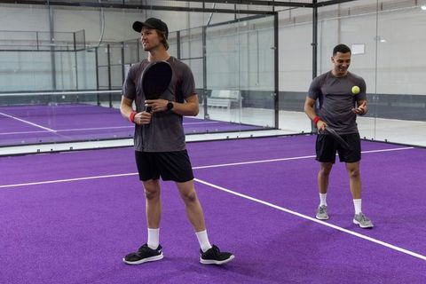 Two men playing padel on vibrant purple indoor court wearing gray athletic apparel