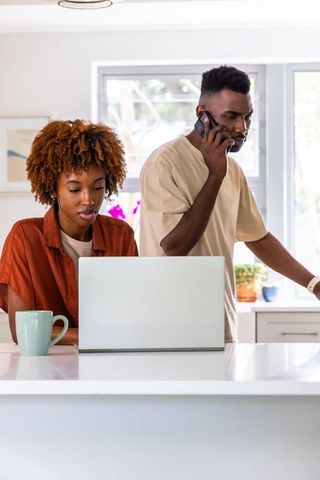 African american couple working from home in bright modern kitchen using laptop and phone