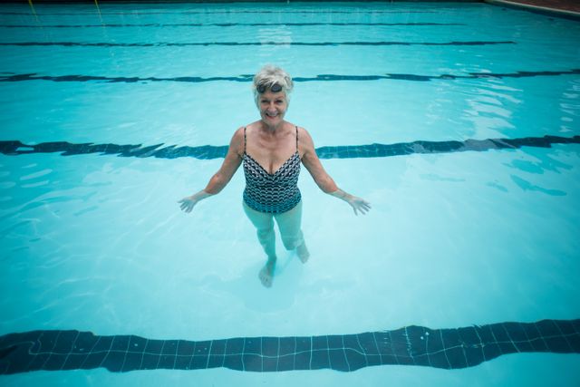 Senior woman swimming in pool, smiling and enjoying her time. Perfect for promoting active lifestyles for seniors, health and wellness campaigns, fitness programs, and leisure activities for the elderly.
