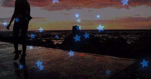 Silhouette woman walking along wet seawall at sunset with star overlays and reflections