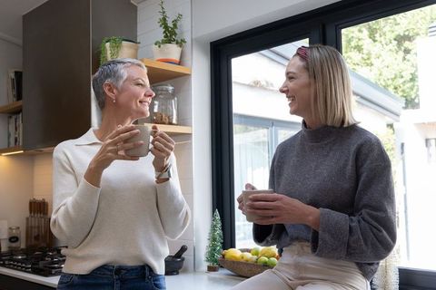 Sharing coffee and conversation in sunlit home kitchen between senior and adult women