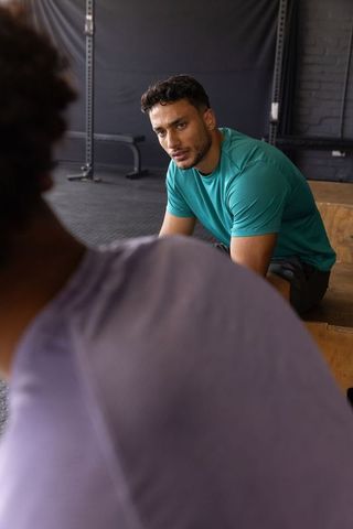 Male workout partners leaning and listening to coaching tips on wooden plyometric box
