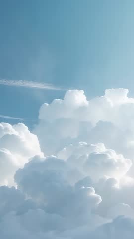 Vertical video: Cumulus clouds billowing across sunlit blue sky with passing contrail
