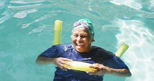 Smiling senior woman enjoying time in swimming pool while floating on pool noodle. Perfect for themes related to healthy aging, outdoor activities, summertime fun, senior fitness, and joyful moments.