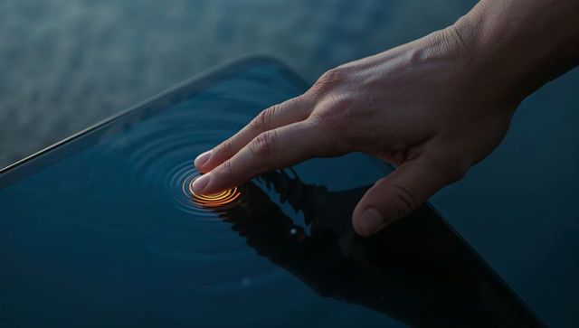 Hand touching glossy screen creating glowing orange ripple ring, futuristic technology