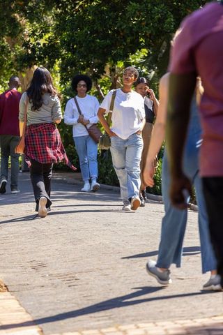 Diverse students walking sun-dappled campus path, african descent woman strolling to camera