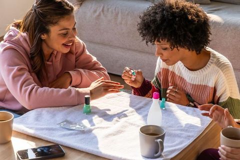 Multiracial friends applying mint-green nail polish during cozy home manicure gathering