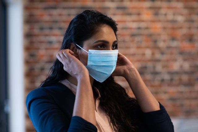 Biracial woman working in a casual office, wearing face mask. Social distancing in the workplace during Coronavirus Covid 19 pandemic.