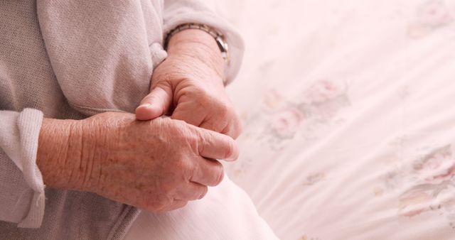 Close-up of elderly person's hands clasped in lap, suggesting a moment of rest and comfort at home. This image can be used for themes of aging, retirement, elderly care, health, and family support, ideal for blog posts, articles, brochures, and websites focused on senior lifestyle and well-being.