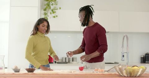 Diverse couple preparing dough together at modern kitchen island, cracking eggs
