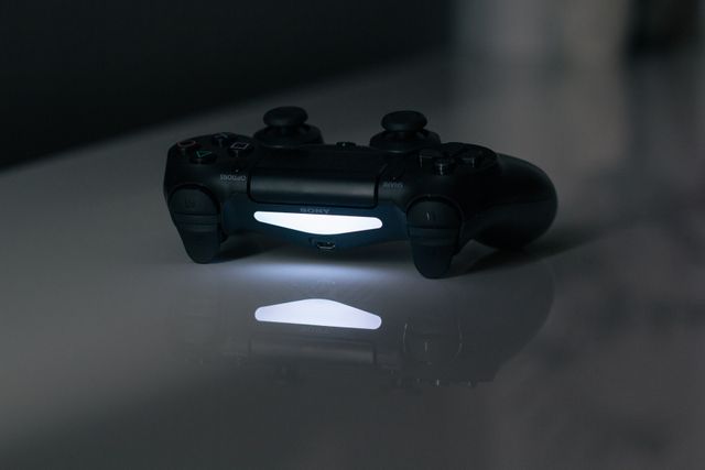 Glowing video game controller reflecting on smooth surface in dark room emitting soft light. Suitable for articles about gaming, technology, video game equipment, or night gaming setups.