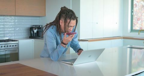 Midadult african american man leaning on kitchen island speaking into phone with laptop