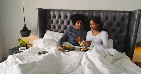 Couple sharing breakfast in bed with croissants, modern headboard and cozy morning vibes