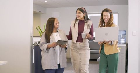 Diverse female coworkers walking and collaborating in modern office corridor