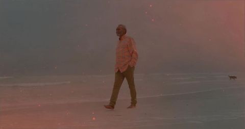 Senior man walking barefoot on ocean shore at dusk