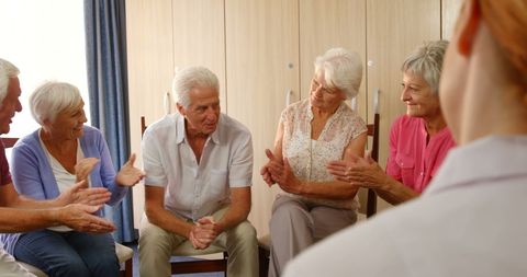 Senior friends applauding enthusiastically in bright living room