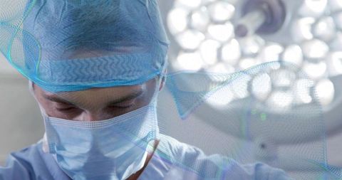 Senior surgeon concentrating in operating room wearing surgical mask cap under LED lights