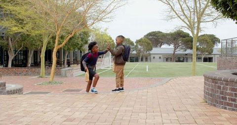 Male Students High-Fiving in School Courtyard Developing Camaraderie
